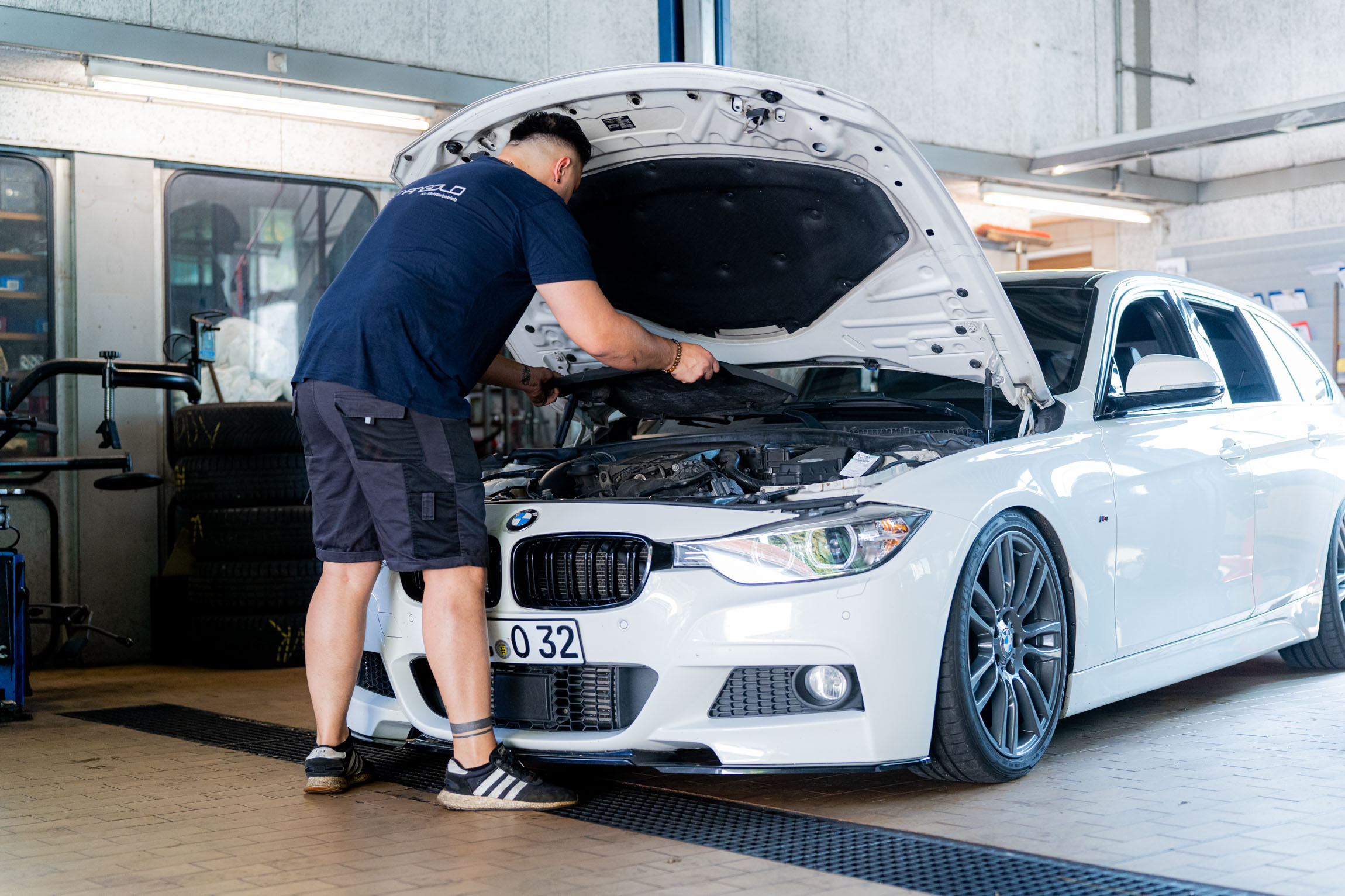 Ein Mann arbeitet in einer Garage an einem BMW-Auto und führt Reparaturen durch.