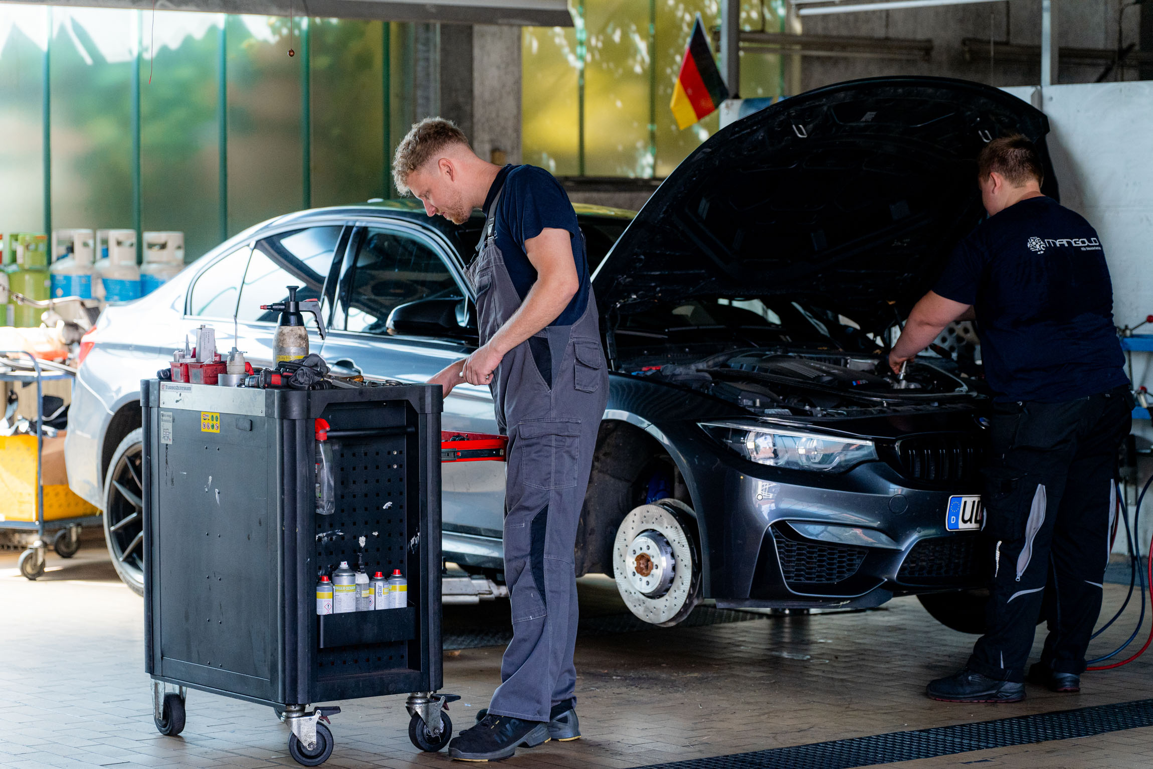 Zwei Männer in einer Garage, die gemeinsam an einem Auto arbeiten und technische Anpassungen vornehmen.