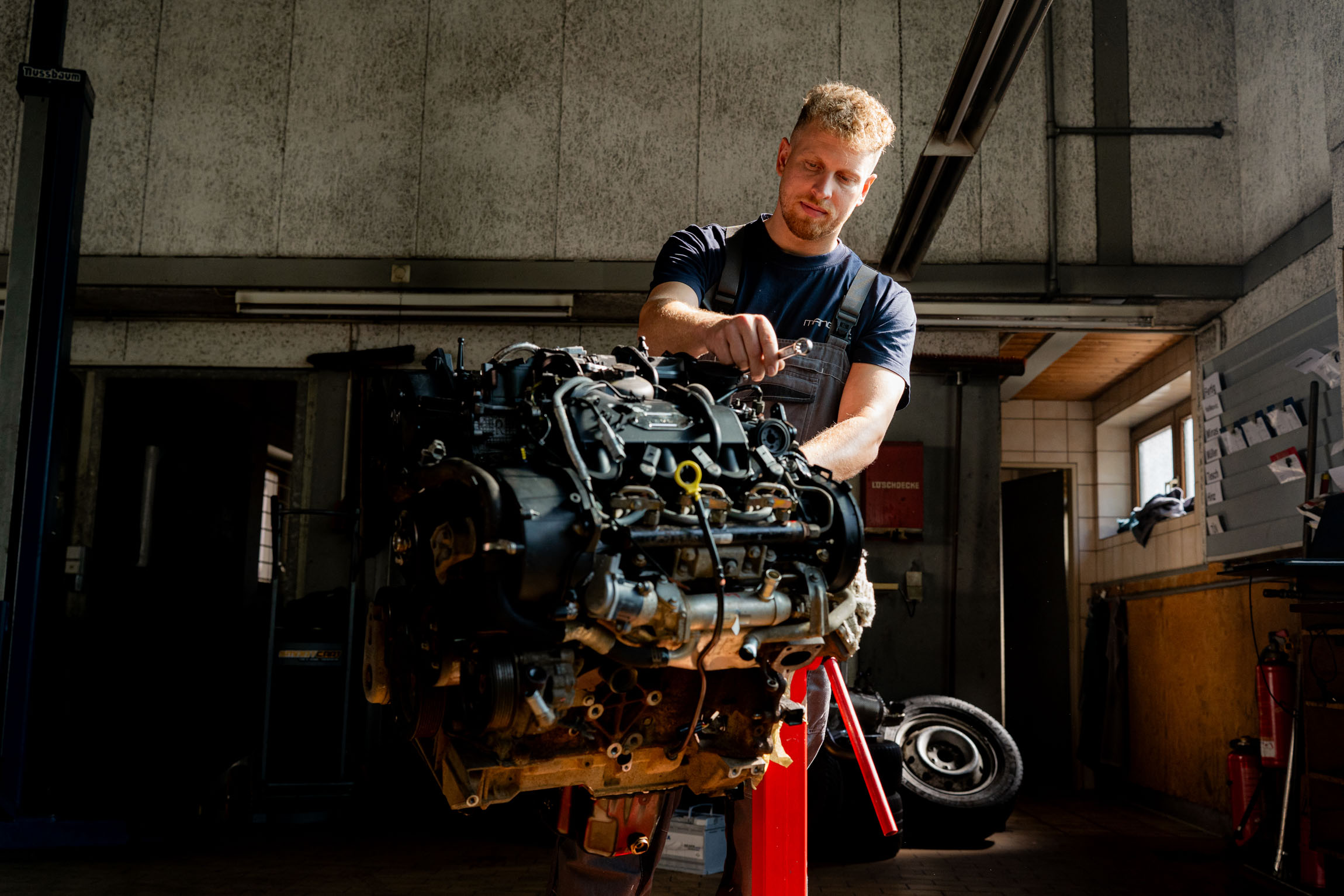 Ein Mann hält einen großen Motor in einer Garage und zeigt dabei seine handwerklichen Fähigkeiten.